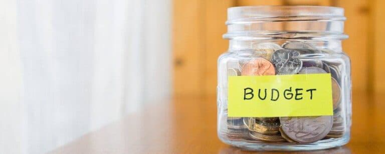 Glass bank with many world coins and budget word or label on saving money jar