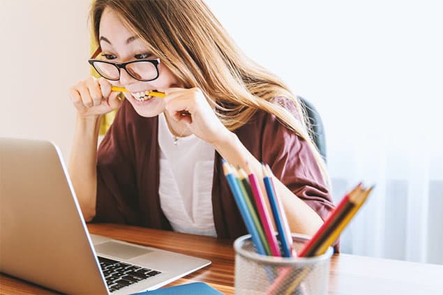 A woman biting a pencil while staring at her laptop screen