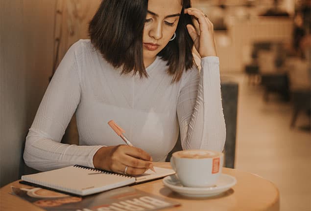 A brunette woman sitting in a cafe writing in her journal